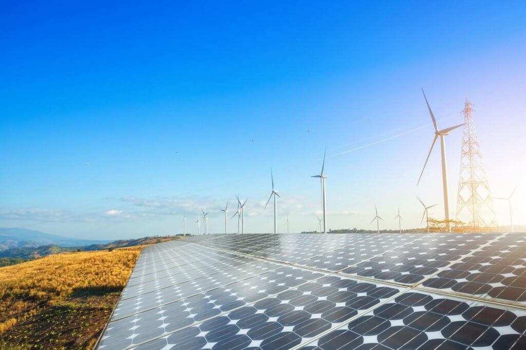 在晴朗的日子里，一排太阳能电池板在一排风力涡轮机和输电塔前面。